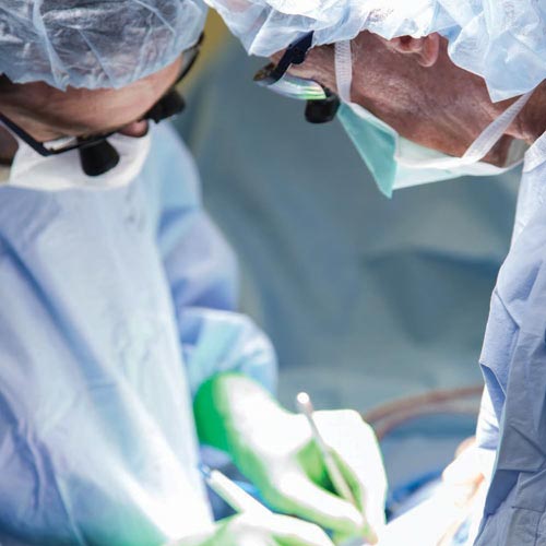 Two surgeons in blue gowns perform a surgery on a patient in an operating room
