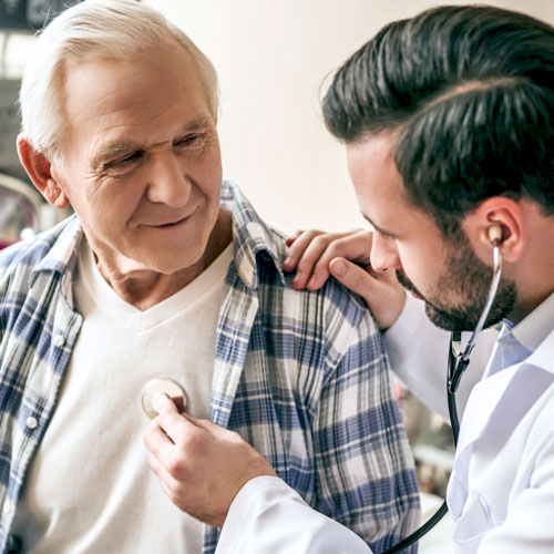 A doctor in a white lab coat uses a stethoscope to check an older male patient