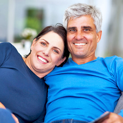 Un hombre y una mujer sonrientes de mediana edad con camisas azules se sientan uno cerca del otro