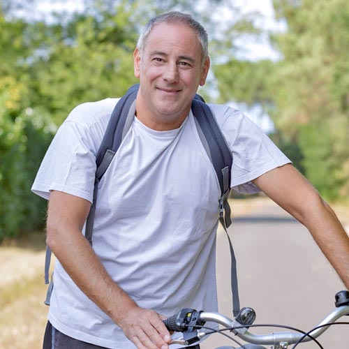 A middle-aged man in a gray T-shirt stands next to his bicycle in the park