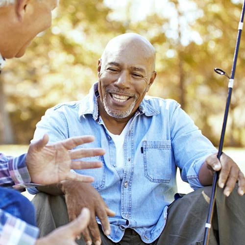 Un hombre con una camisa azul sentado sosteniendo una caña de pescar habla con un hombre mayor