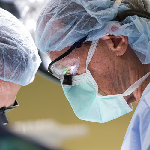 Two vascular surgeons in blue scrubs perform a heart operation in the OR