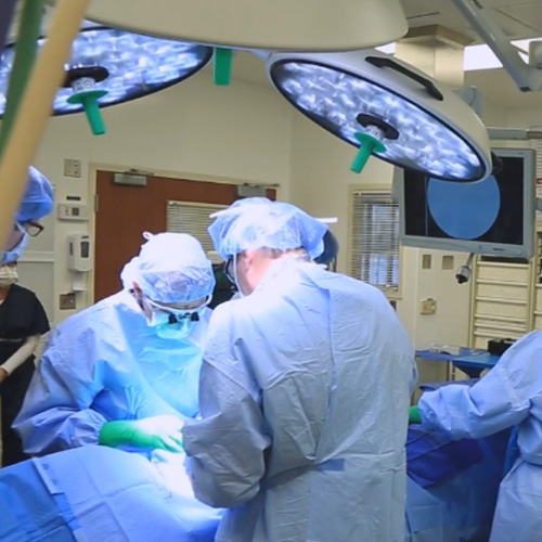 Several vascular surgeons in blue scrubs perform a surgery in the operating room