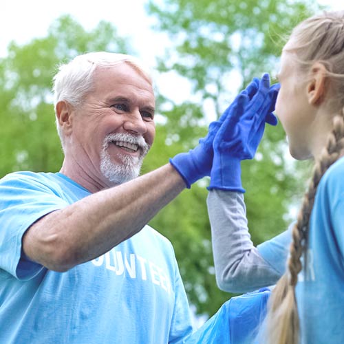 A grandfather in a blue volunteer shirt high-fives his granddaughter