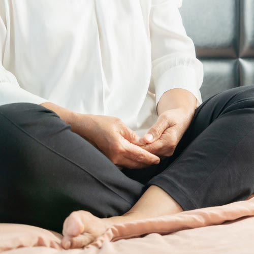 A woman in a white shirt and black pants sits with her legs crossed in a meditation pose