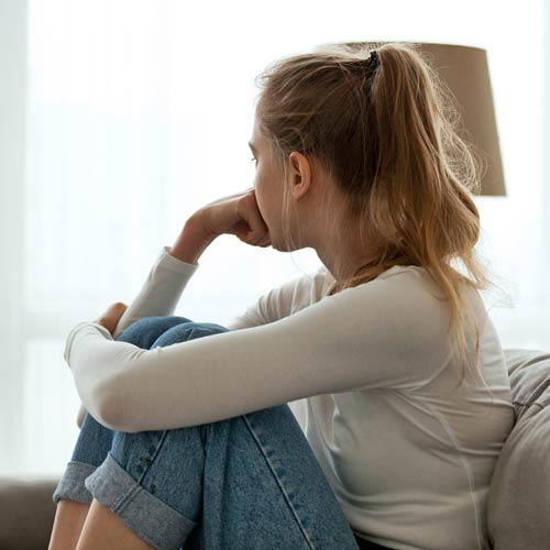 Una mujer sentada en un sofá con las rodillas levantadas mirando hacia otro lado de la cámara
