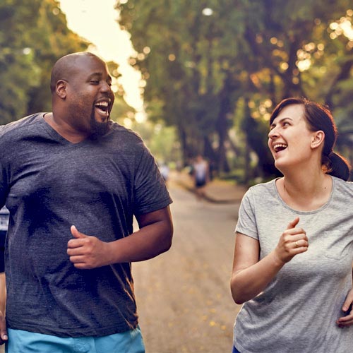 A man and a woman smile at each other while running in a neighborhood