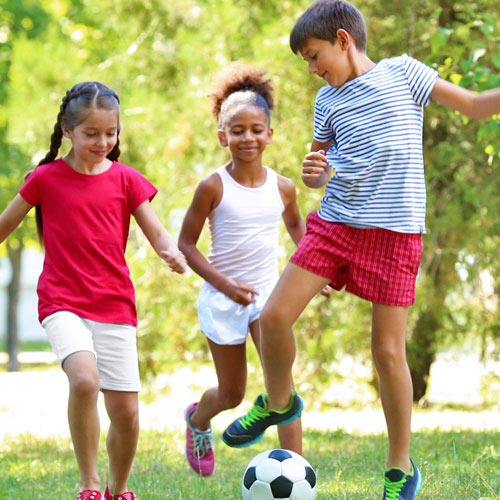 Three children play soccer in the park