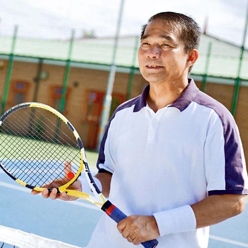 A man stands at the net of a tennis court holding a tennis racquet.