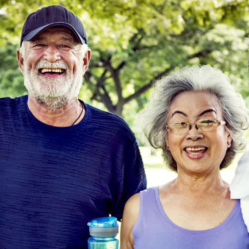 A man holding a water bottle stands next to a woman in the park, both are smiling and happy