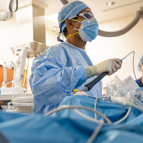 A cardiac surgeon in blue scrubs in the operating room performs a minimally invasive heart procedure