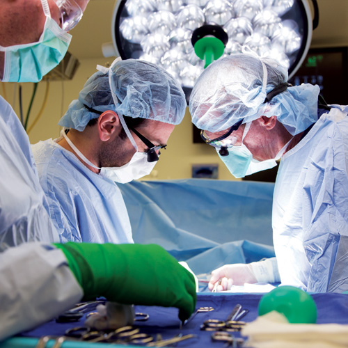 Three vascular surgeons in blue scrubs perform a heart surgery in the operating room