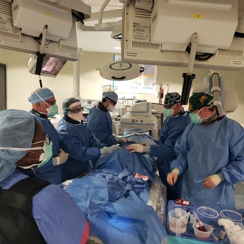 A group of surgeons in blue gowns perform heart surgery in the operating room