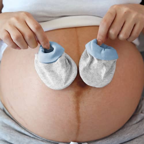 A pregnant mother holds two small baby booties in front of her stomach